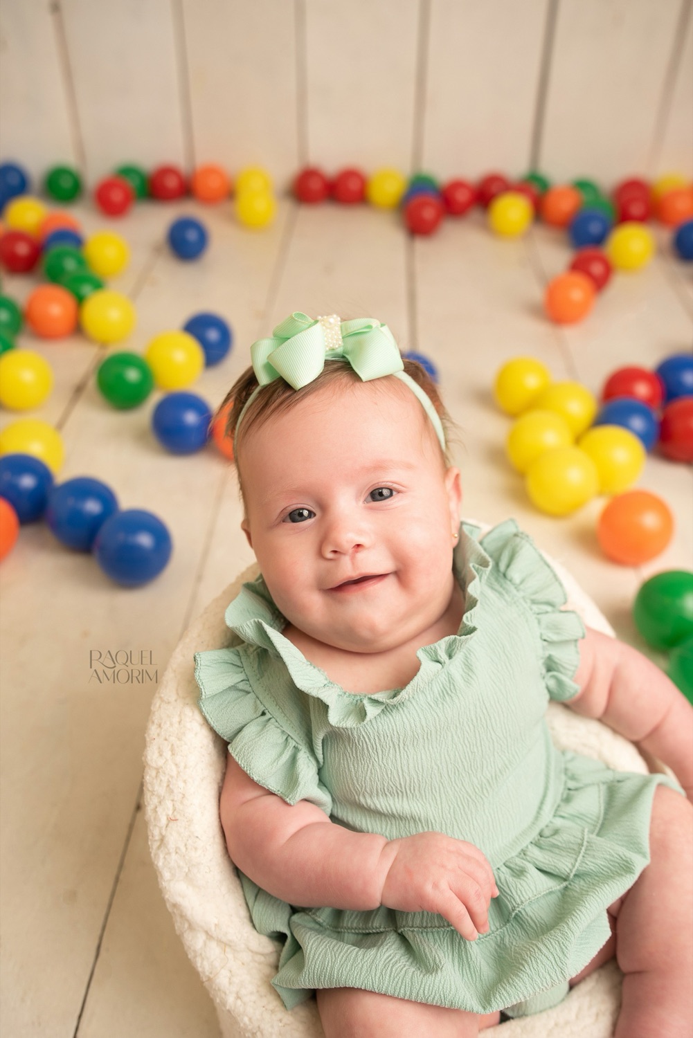 Celine, 3 meses, sorrindo cercada de bolinhas coloridas